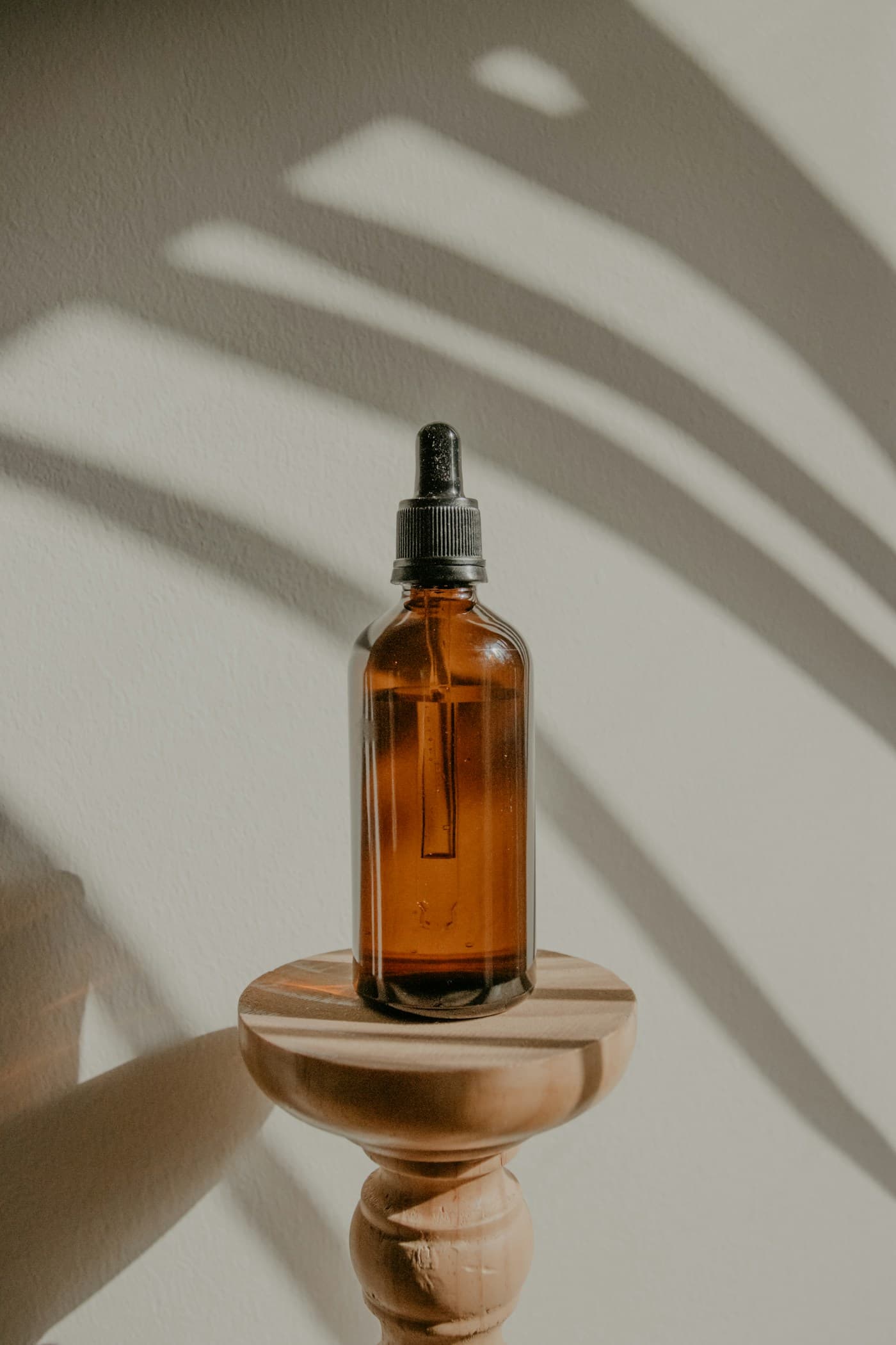An unlabelled amber glass dropper bottle on a wooden stand, lit by window shadow.