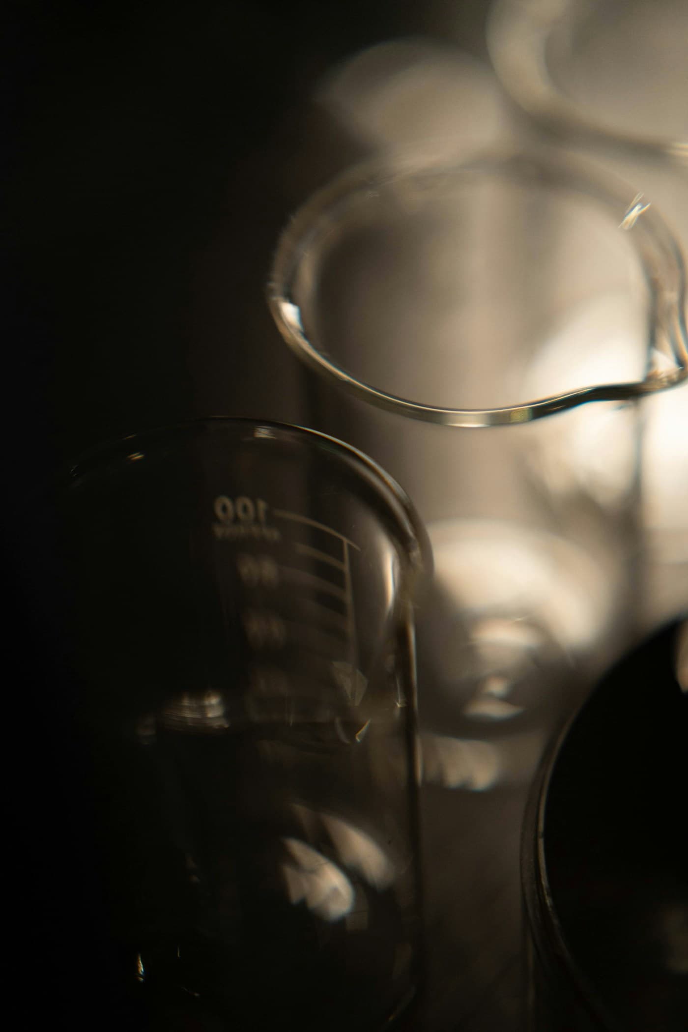 Graduated laboratory beakers backlit against a dark background, volume markings visible.